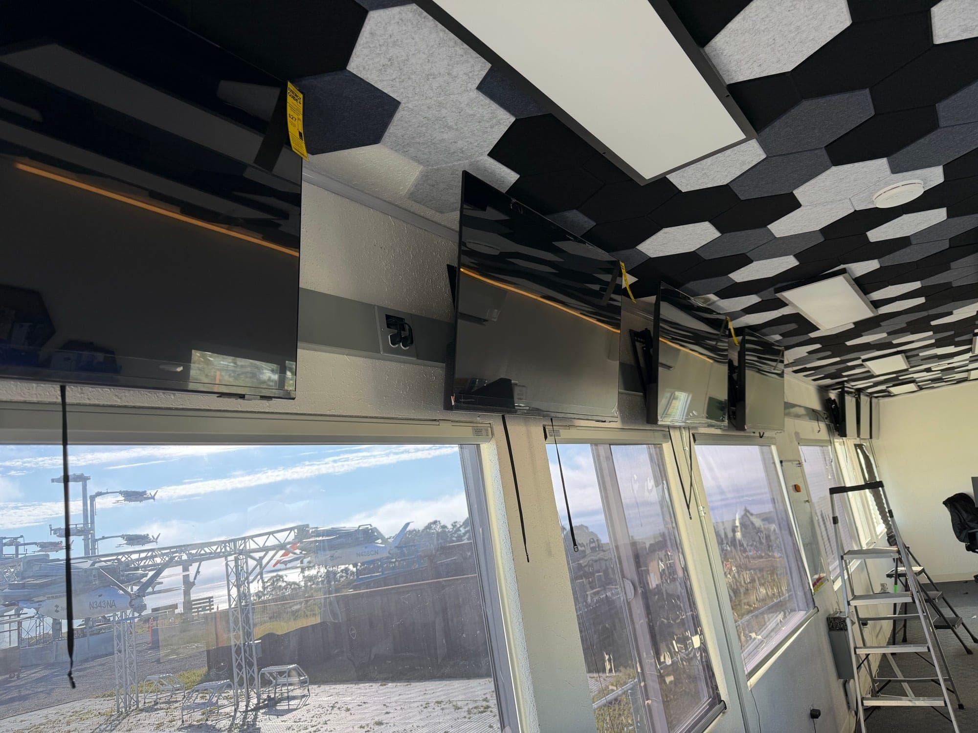 A row of large flat screen displays mounted in a level line along an office wall above the windows
