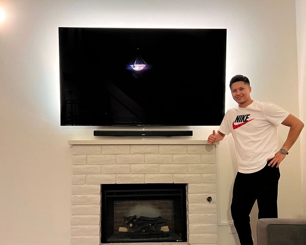 A large flat screen TV mounted above a white painted brick fireplace with a soundbar below it