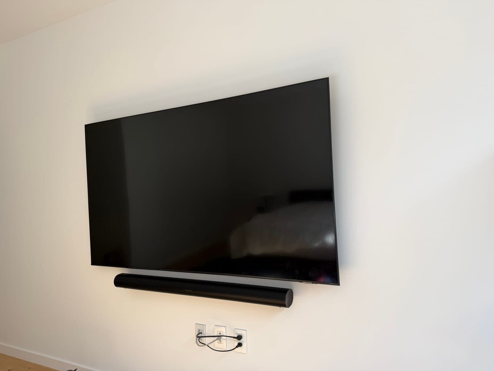 A close-up of a wall-mounted TV and soundbar with a single thin cable running to a recessed low-voltage plate