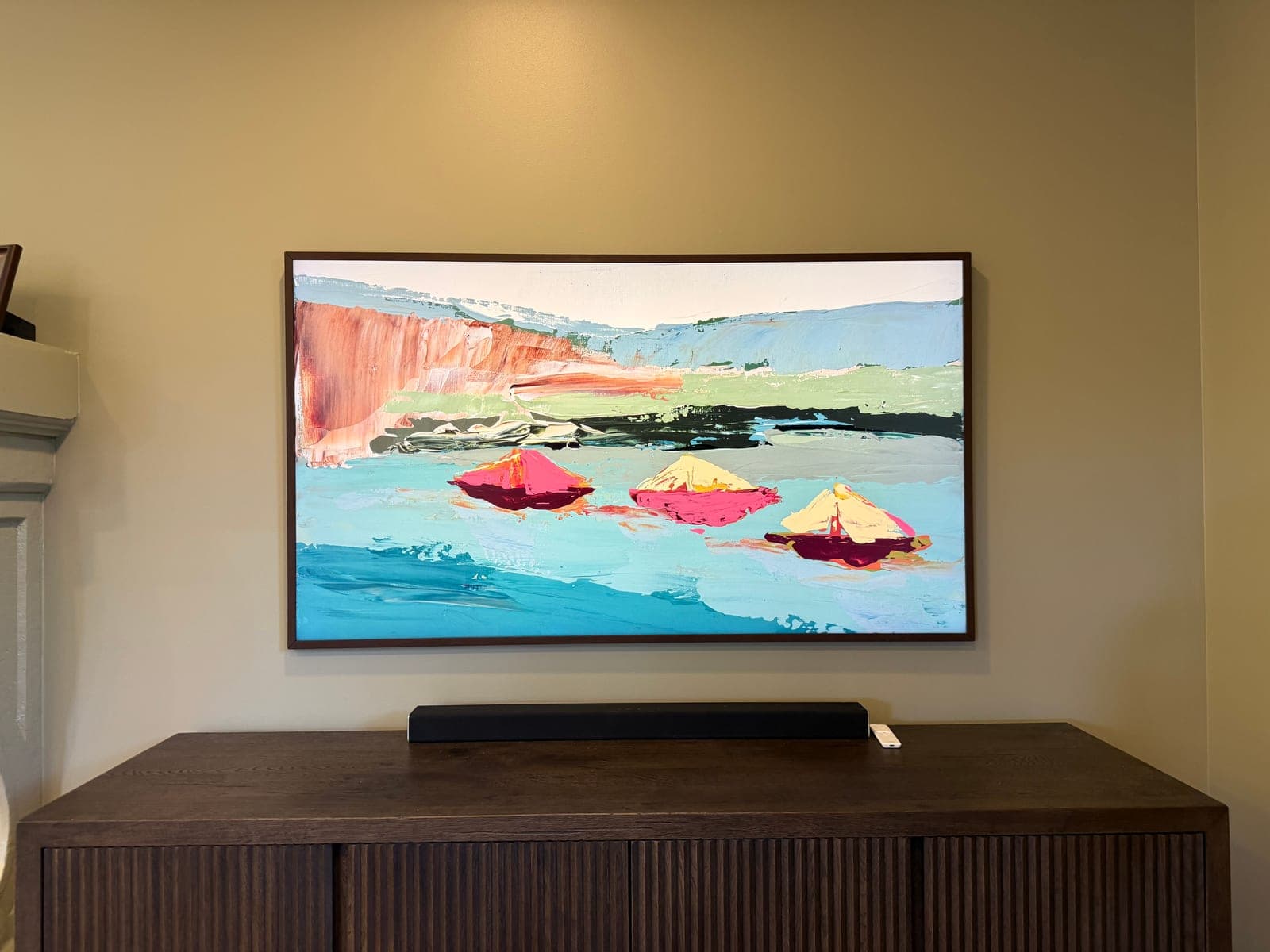 A Frame TV in art mode showing a painting, mounted above a dark wood credenza