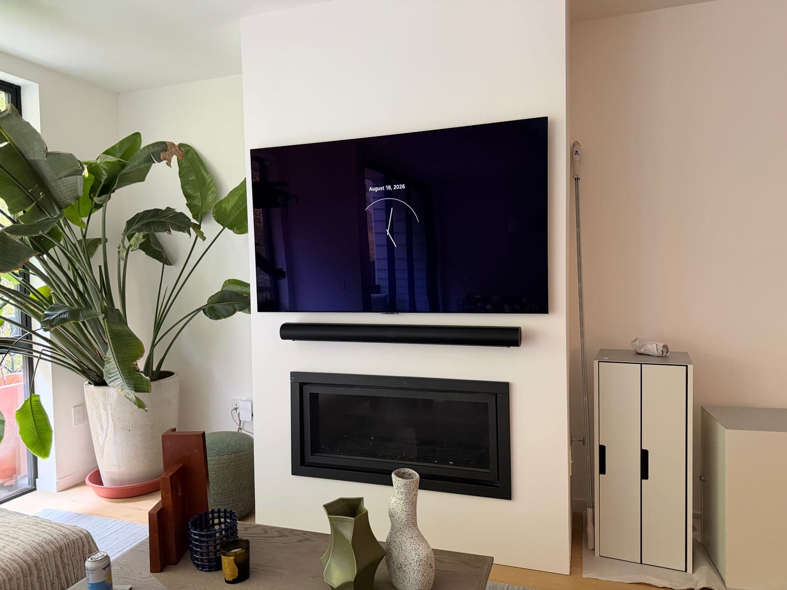 A styled living room with a flat screen TV and soundbar mounted above a modern linear fireplace