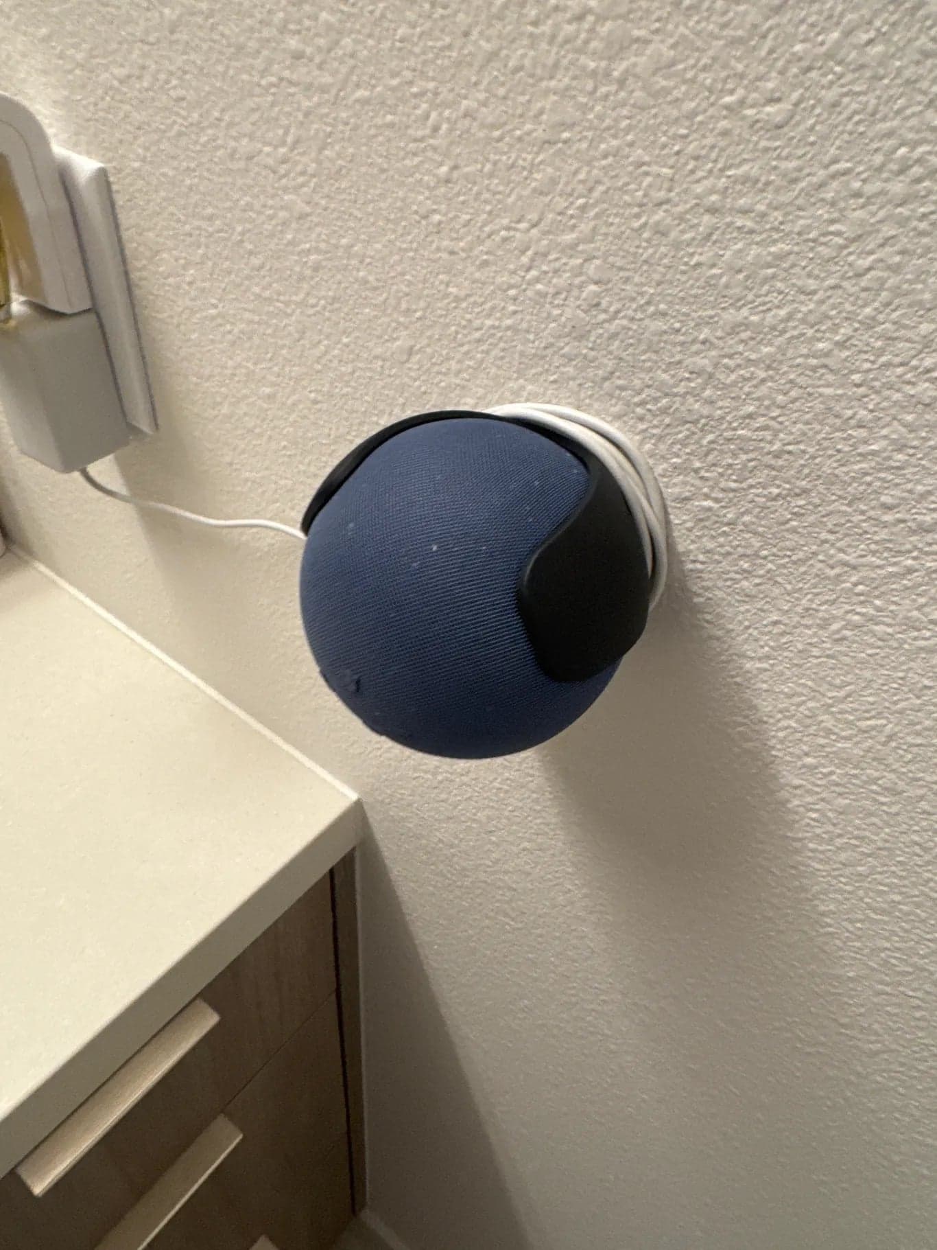 A small round smart speaker mounted on the wall above a bathroom counter