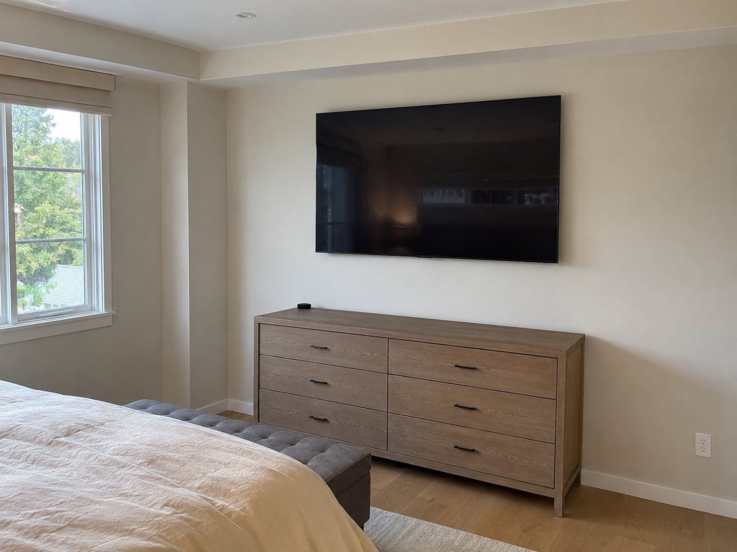 A flat screen TV mounted above a dresser in a bedroom