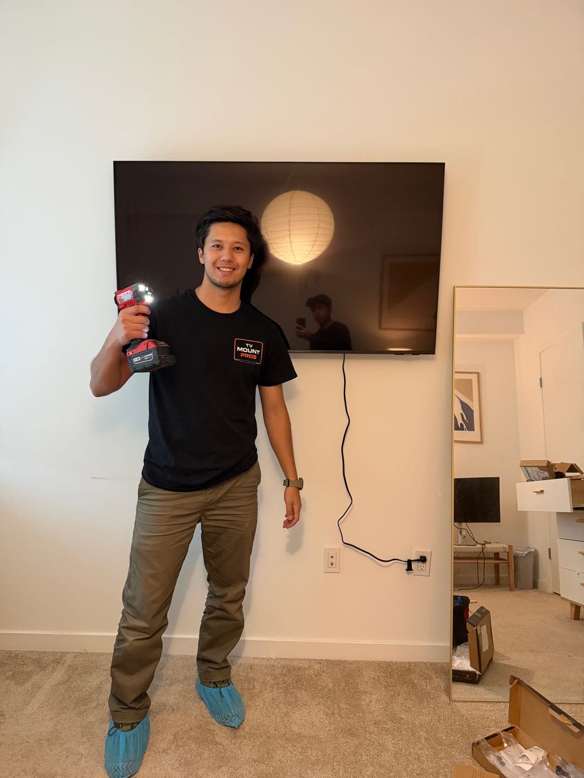 A team member holding a drill and smiling next to a freshly wall-mounted flat screen TV