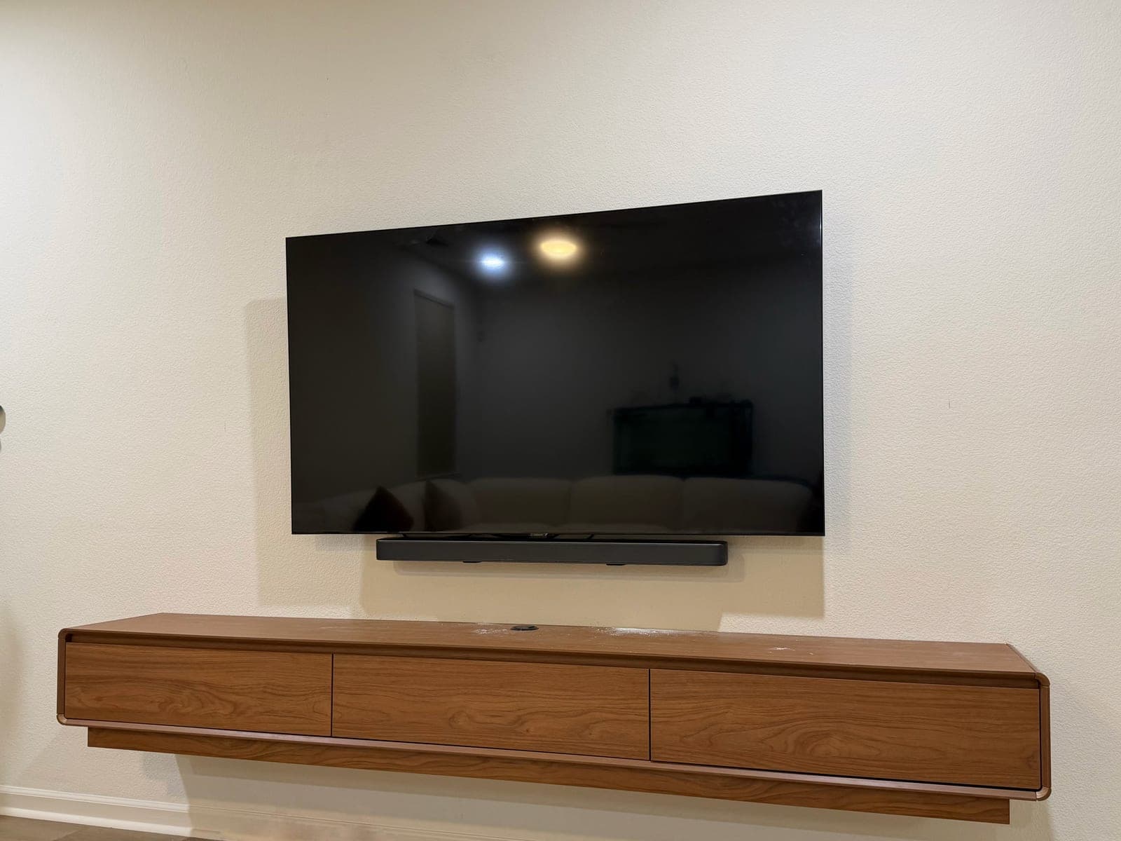 A flat screen TV and soundbar mounted above a floating walnut credenza