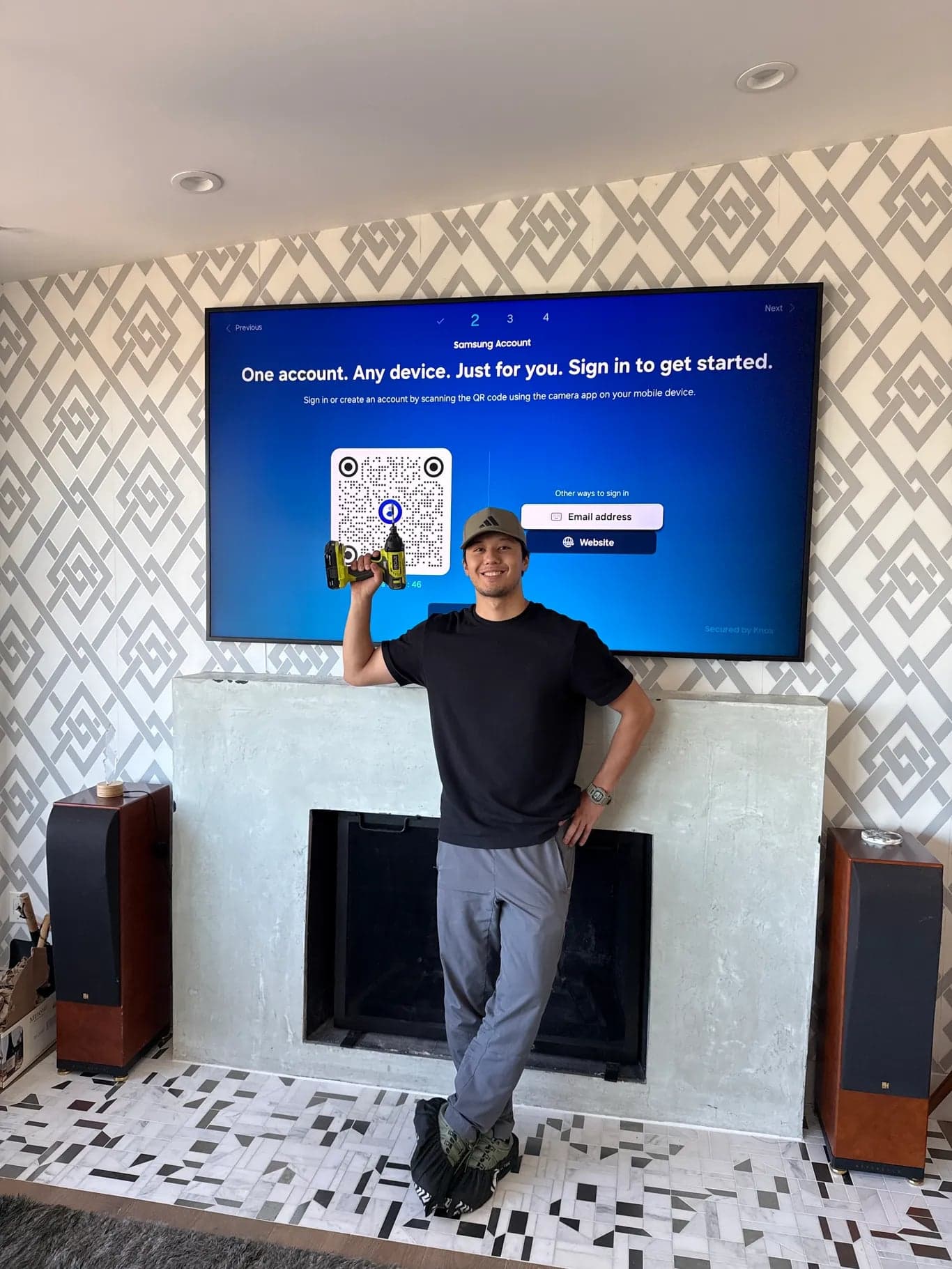 A flat screen TV mounted above a concrete mantel on a wallpapered wall