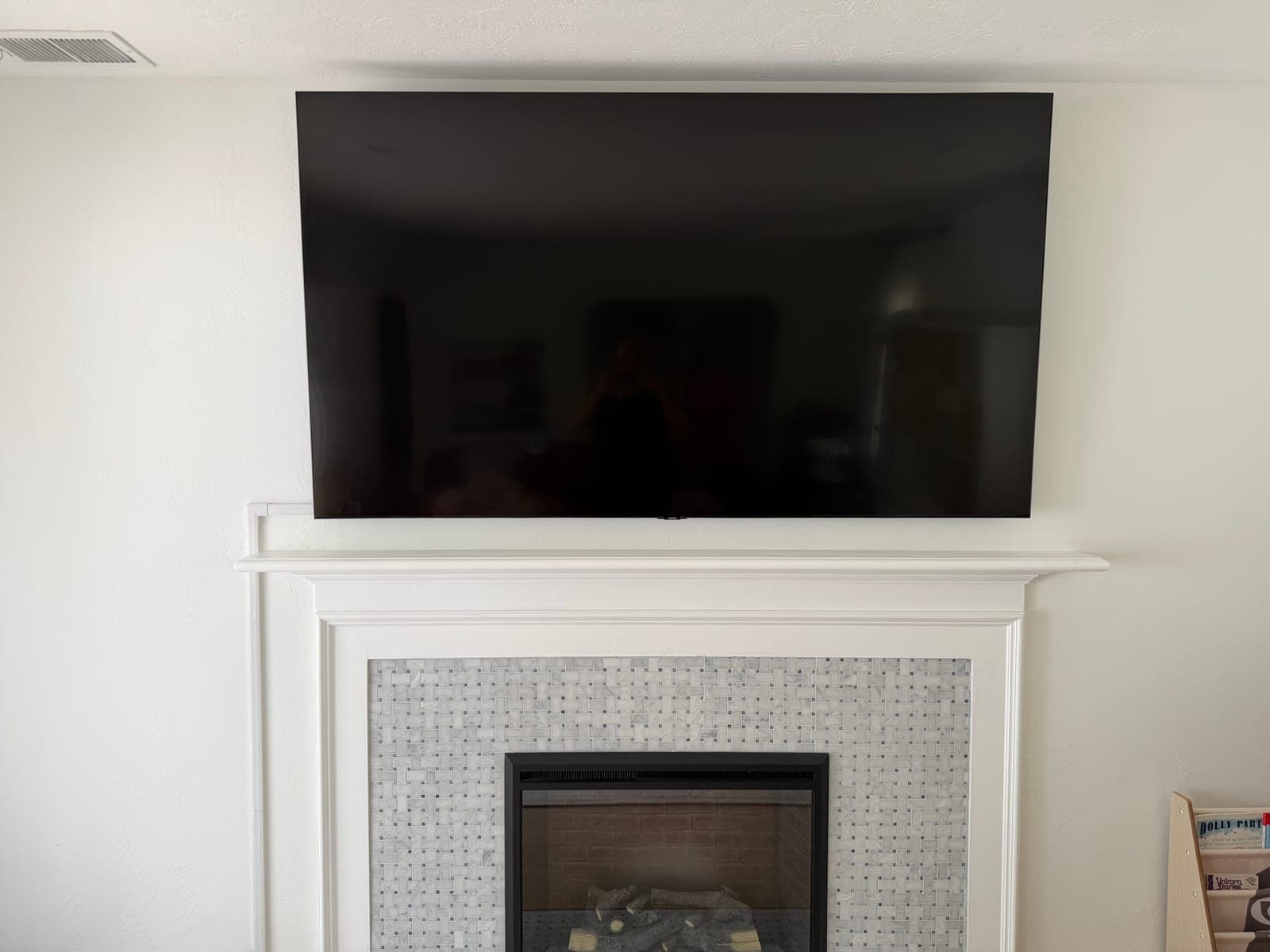 A flat screen TV mounted above a classic white mantel with basket-weave tile surround